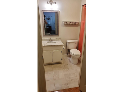 A clean bathroom with stone tile floor, a marbled sink top, new silver faucet, new mirror, and new light fixture