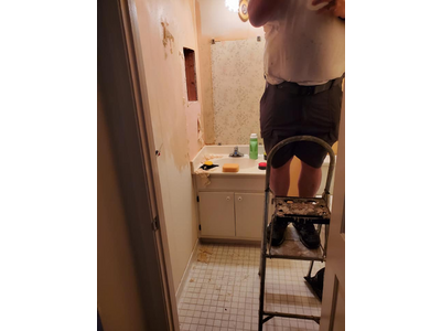 A bathroom with worn small-tiled floor. Old wall treatments are in the process of being removed.