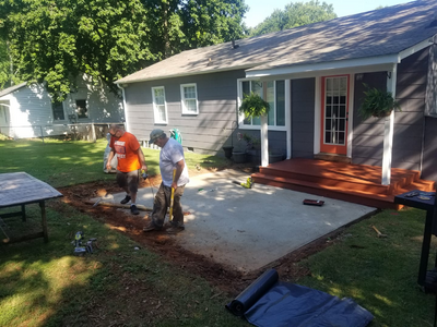 A small red porch with a bare concrete area in front of it. The surrounding lawn is of a higher elevation, and the transition area is under construction.