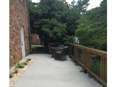 A freshly finished concrete porch with wood and iron railings, plant bed, and furniture
